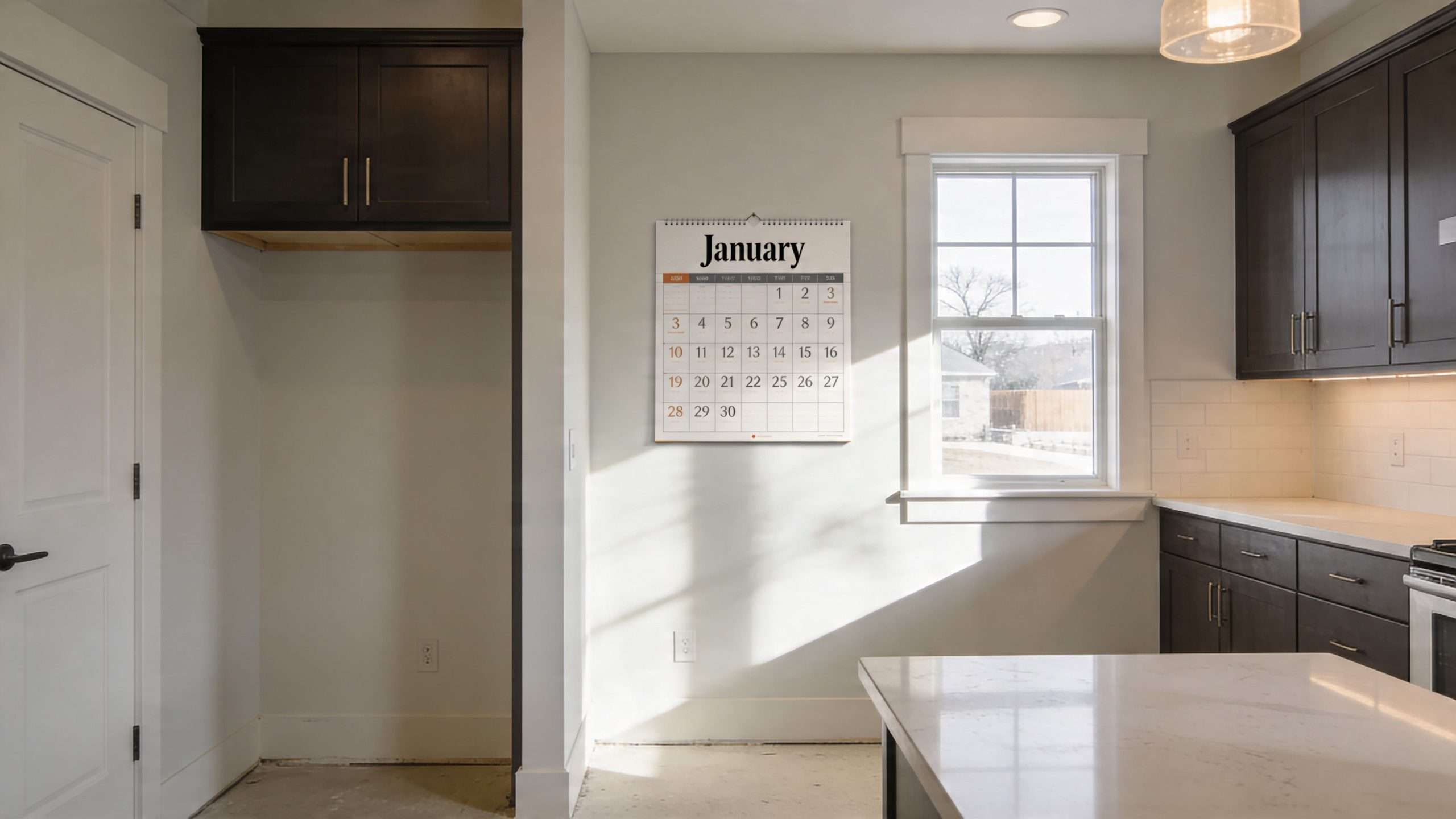 A modern kitchen interior showing dark cabinets, white walls, and a January calendar hung on the wall.